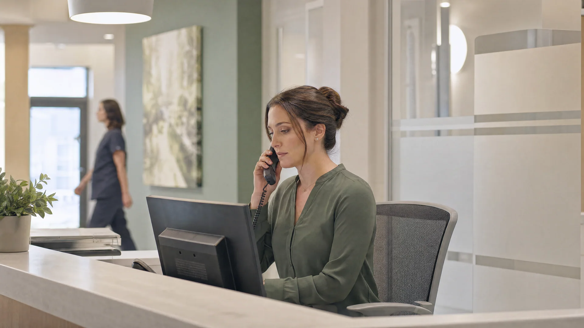 A clinic administrator coordinates an appointment from a quiet reception desk.