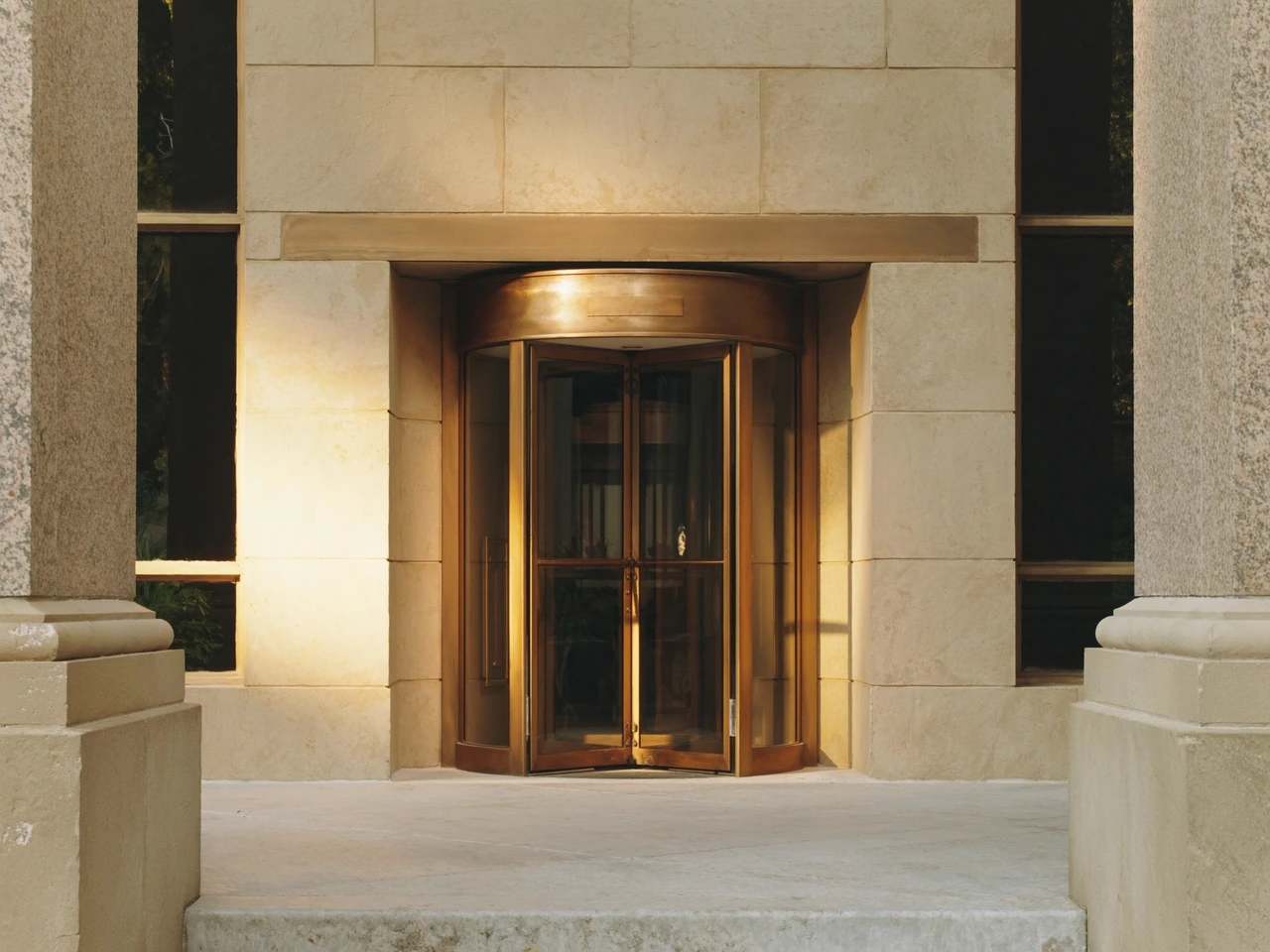 Entrada ilustrativa de un banco de piedra con puerta giratoria de bronce al sol de la tarde.